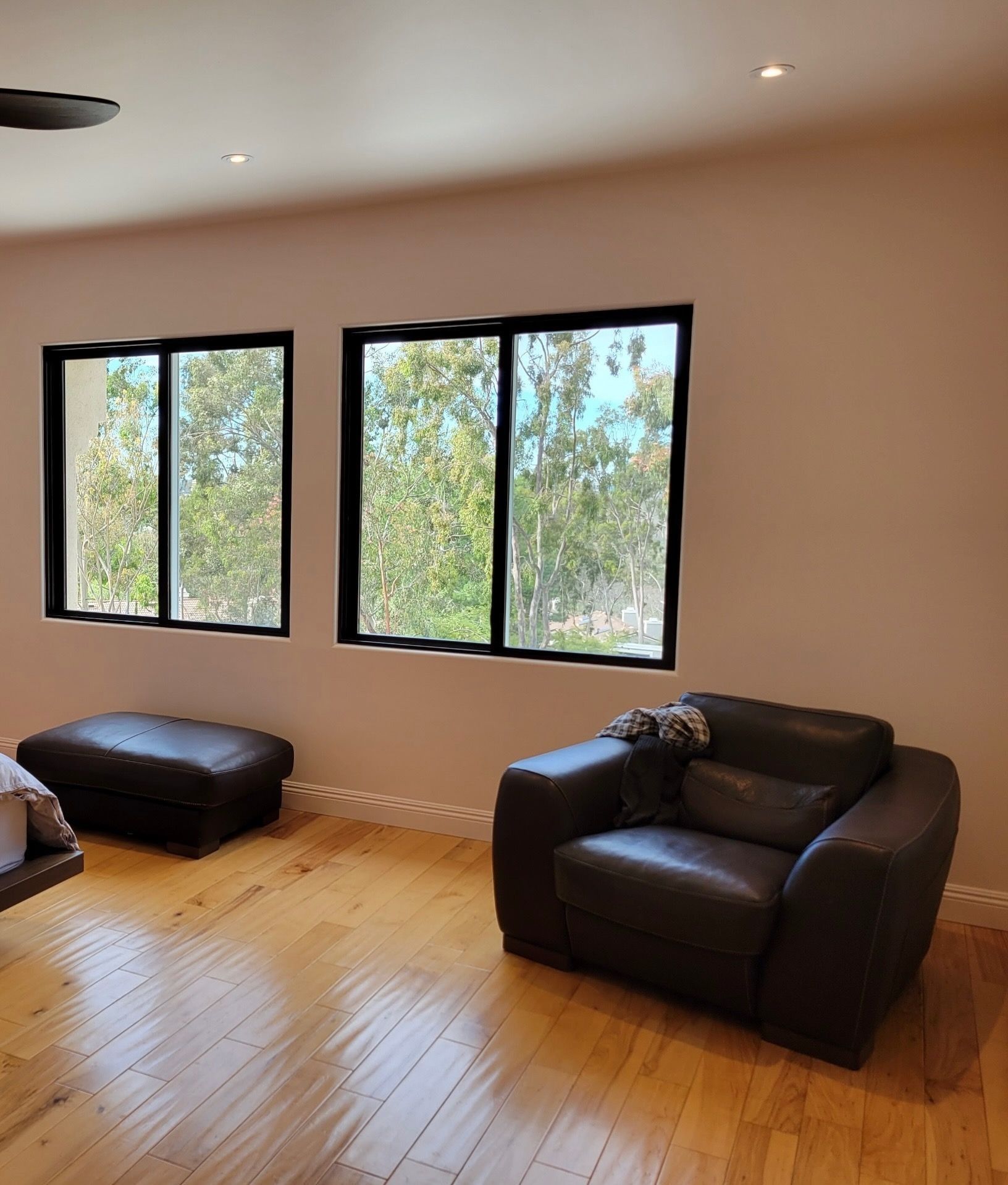 A room with two black-framed windows, a leather armchair, and an ottoman, overlooking a green landscape.