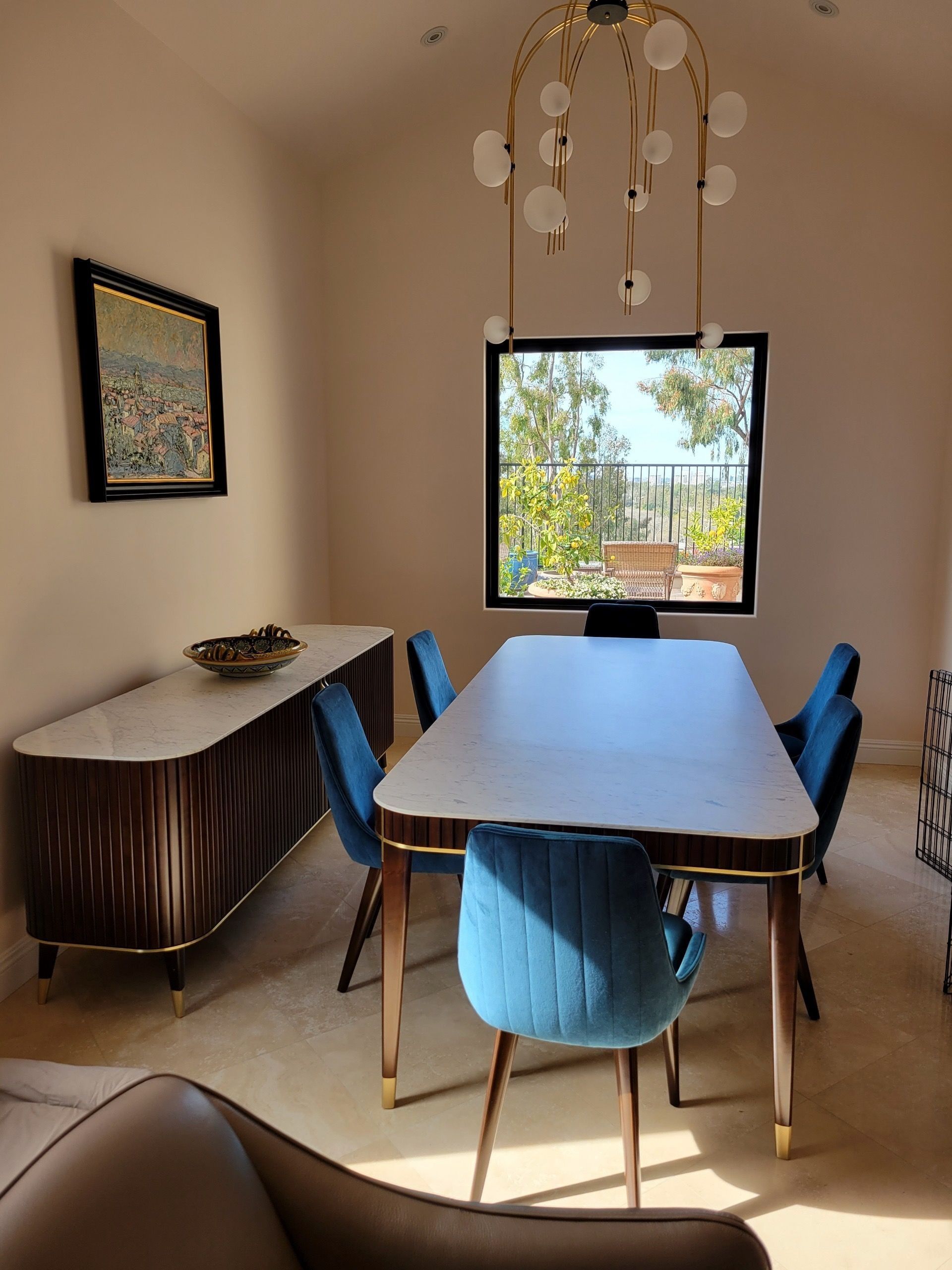 Dining room with blue velvet chairs, marble-topped table and sideboard, and gold chandelier.