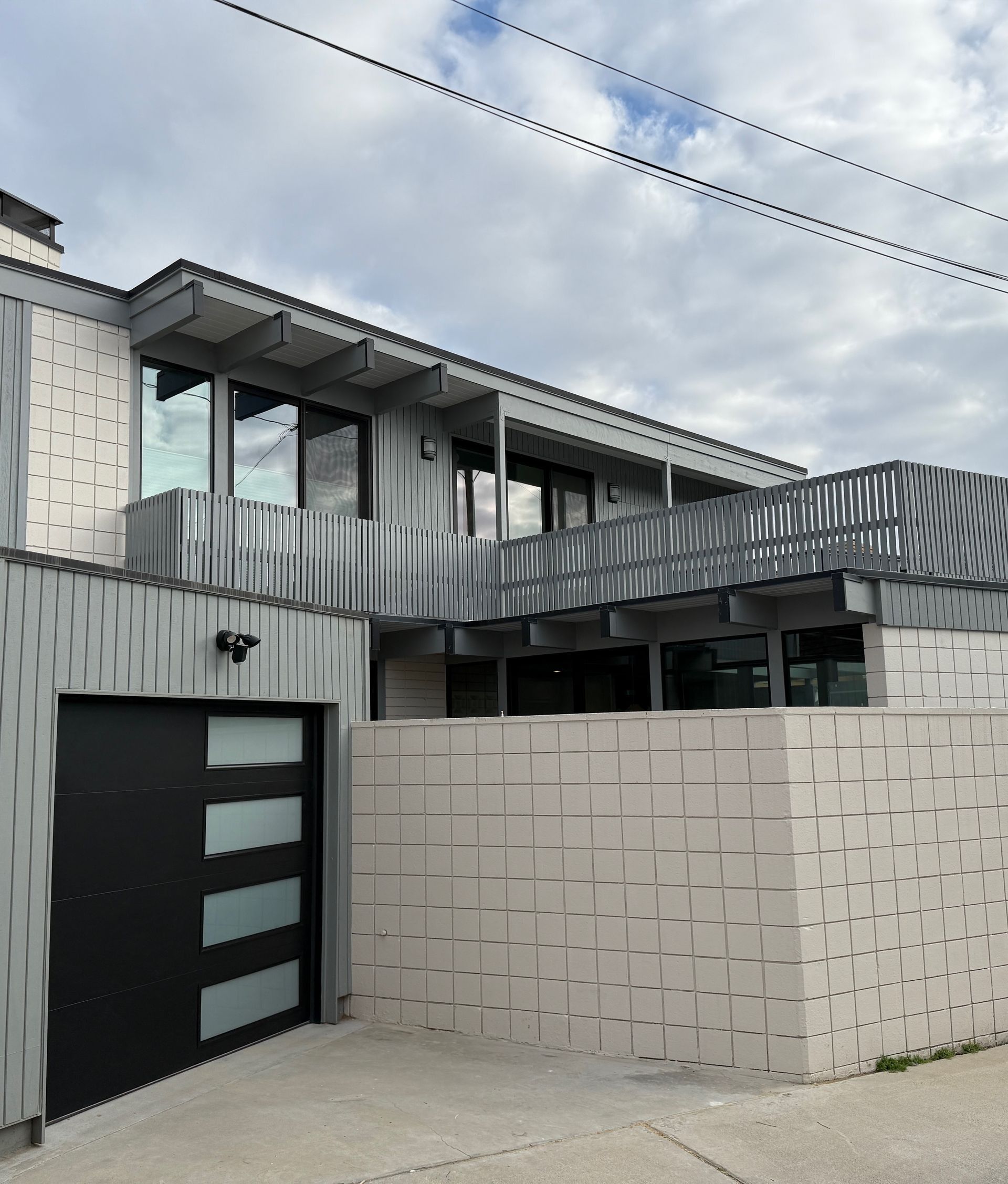 Modern two-story house with gray and white exterior. Black garage door and textured wall.