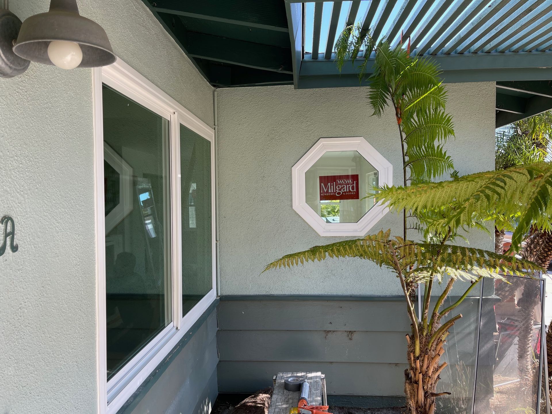 Light blue stucco wall with white-framed windows, an octagon window, and a plant.