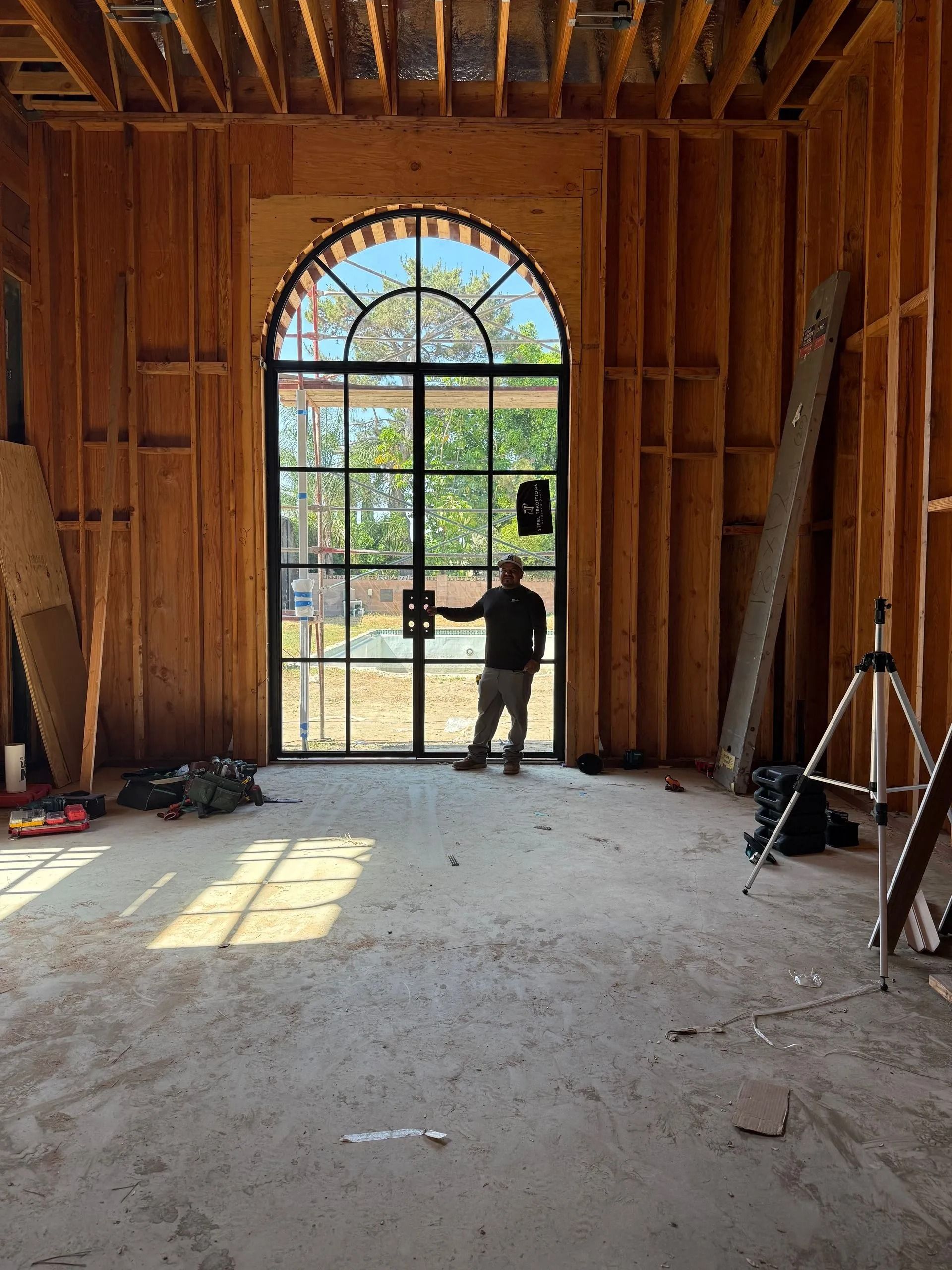Person standing in a room under construction, facing arched glass door. Wood framing visible.
