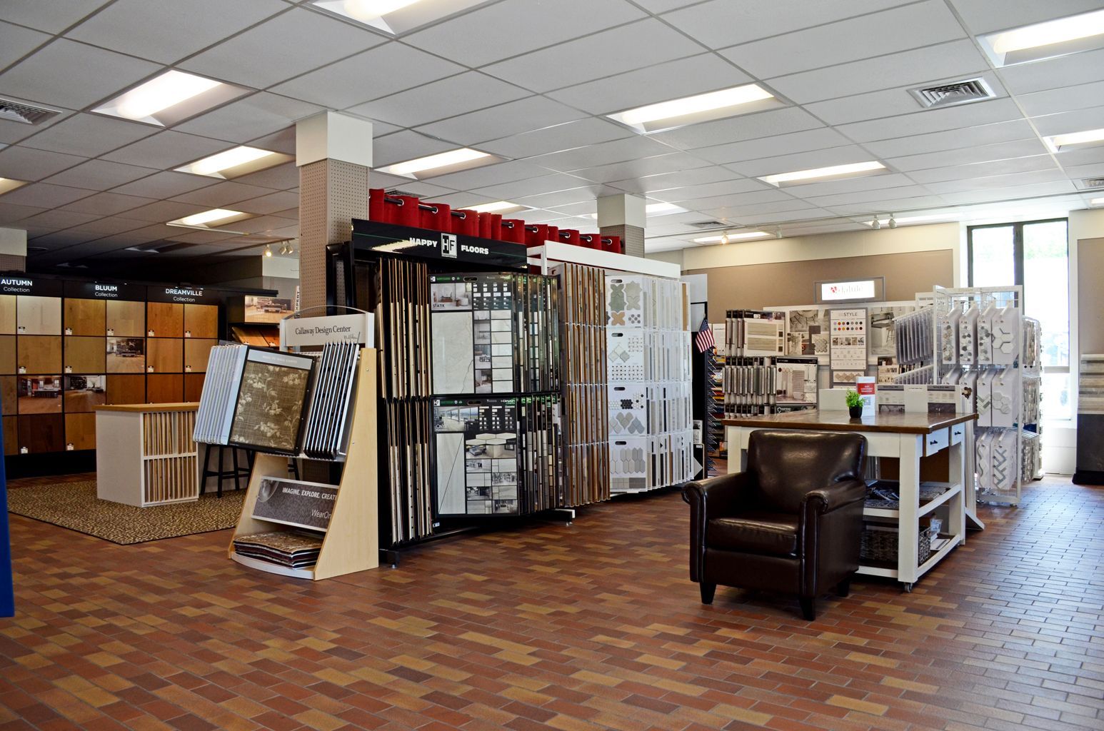 Showroom with flooring and window display samples, cabinets, and a black armchair under bright ceiling lights