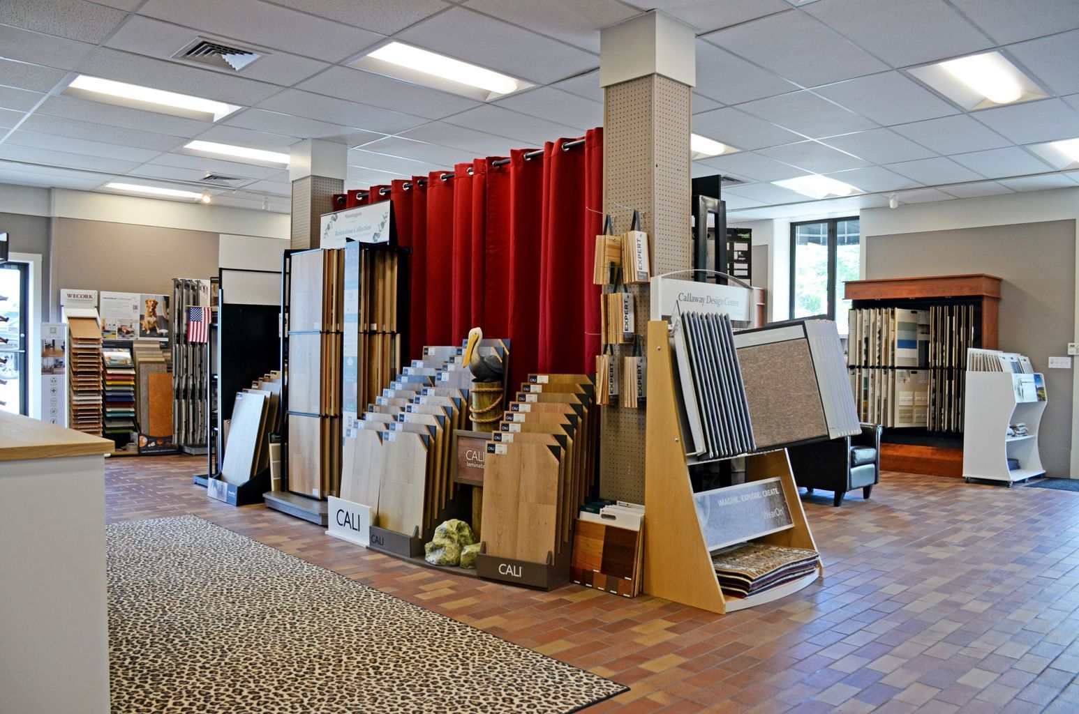 Curtain and flooring showroom with display racks, samples, and red curtains in a bright retail space