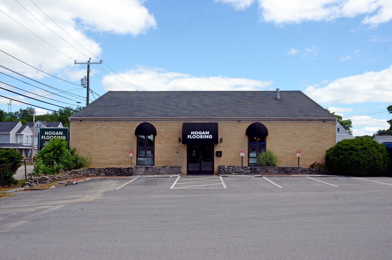Small tan building with black awnings and a sign above the entrance beside an empty parking lot
