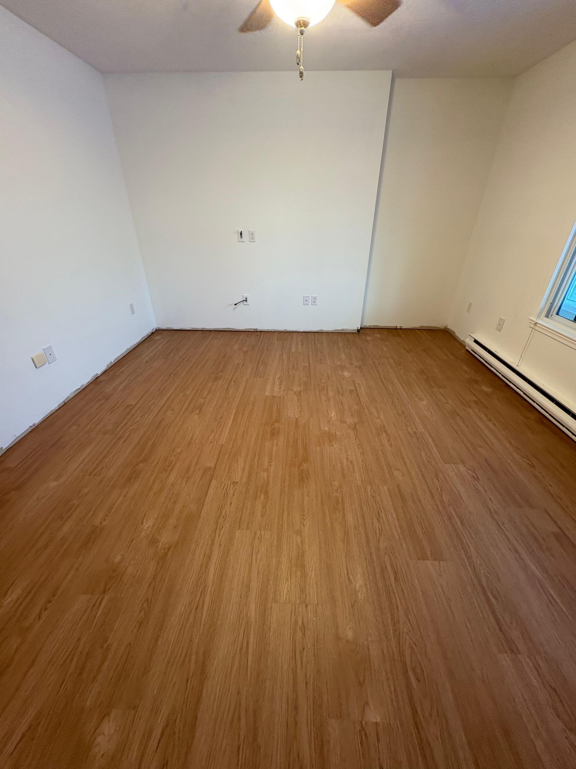 An empty room with light wood-look flooring, white walls, a ceiling fan, and baseboard heating along the right wall.