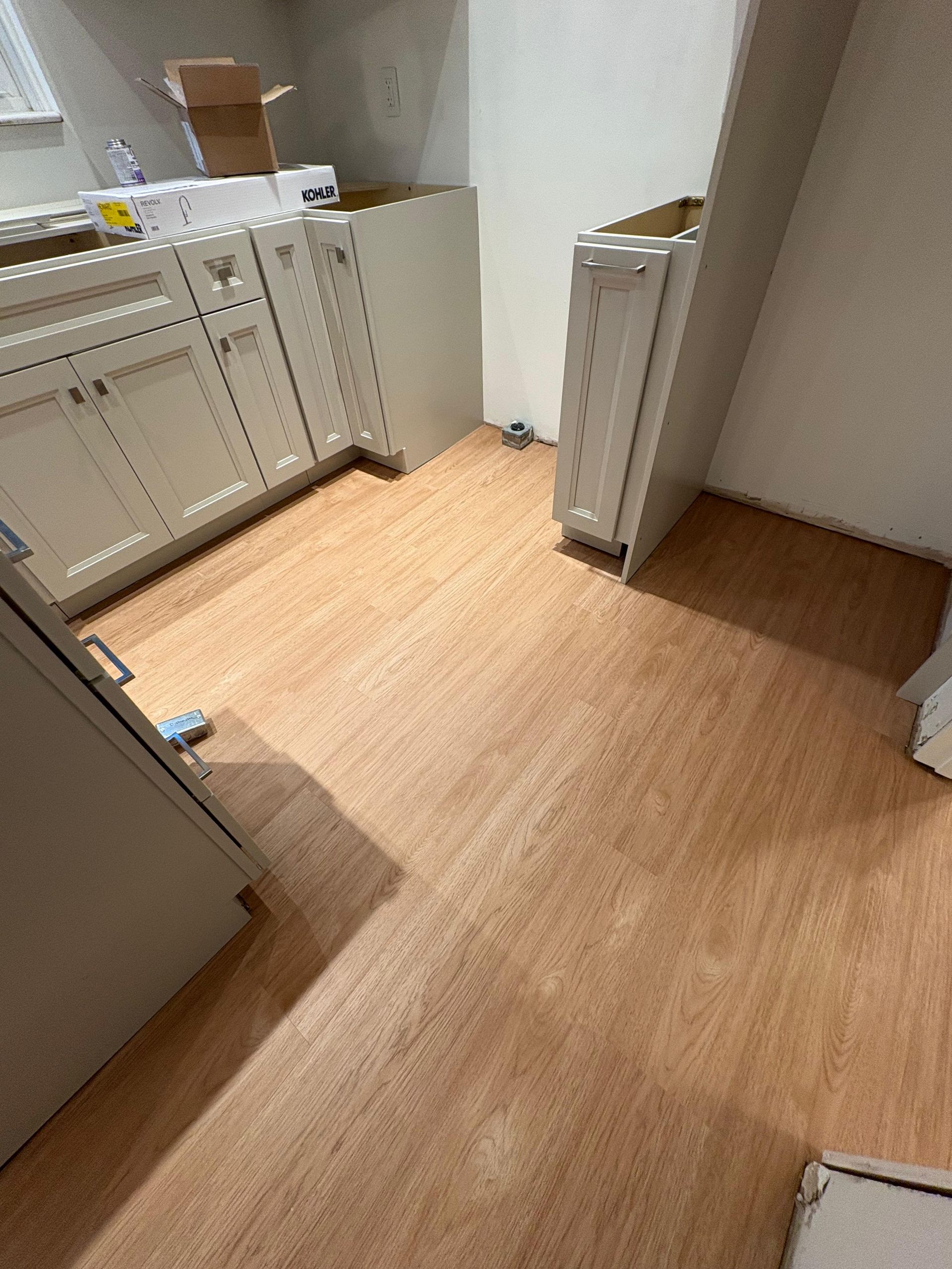 A kitchen undergoing renovation with light-colored cabinets installed on a wood-look vinyl floor.