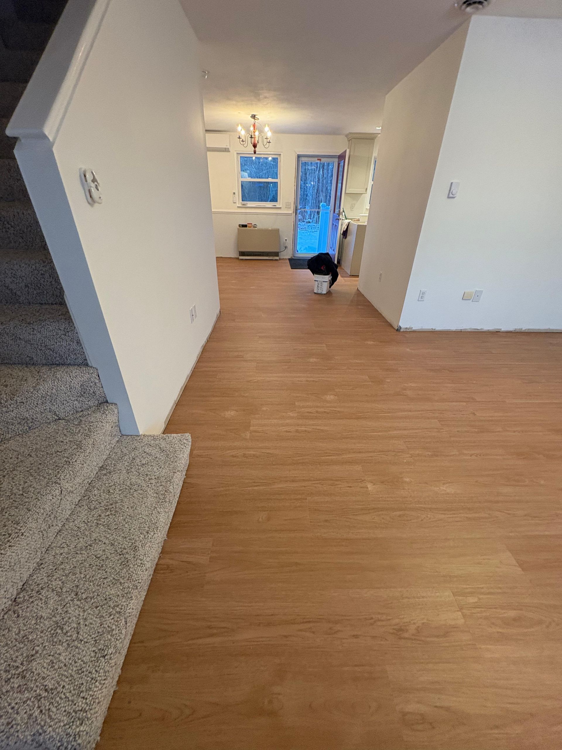 A view from the base of a carpeted staircase looking across wood-look flooring toward a doorway with a glass storm door.