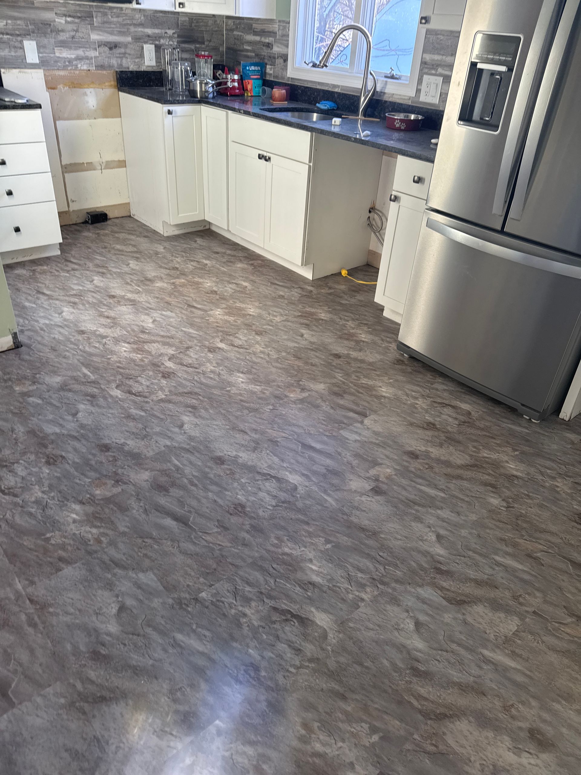 A kitchen with white cabinets, dark countertops, a stainless steel refrigerator, and gray patterned flooring.