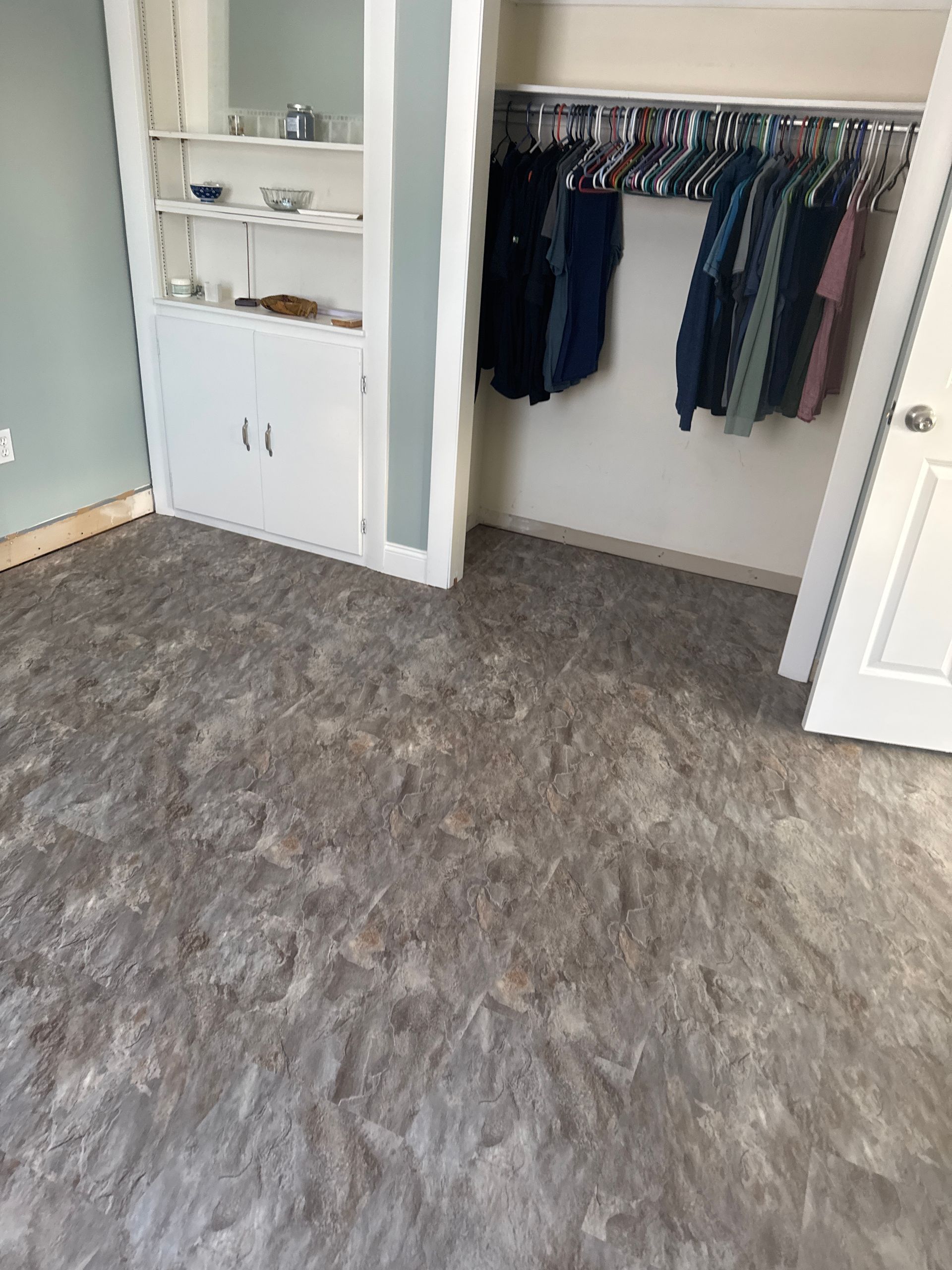 A bedroom featuring light gray textured flooring, a built-in white shelf and cabinet unit, and an open walk-in closet.
