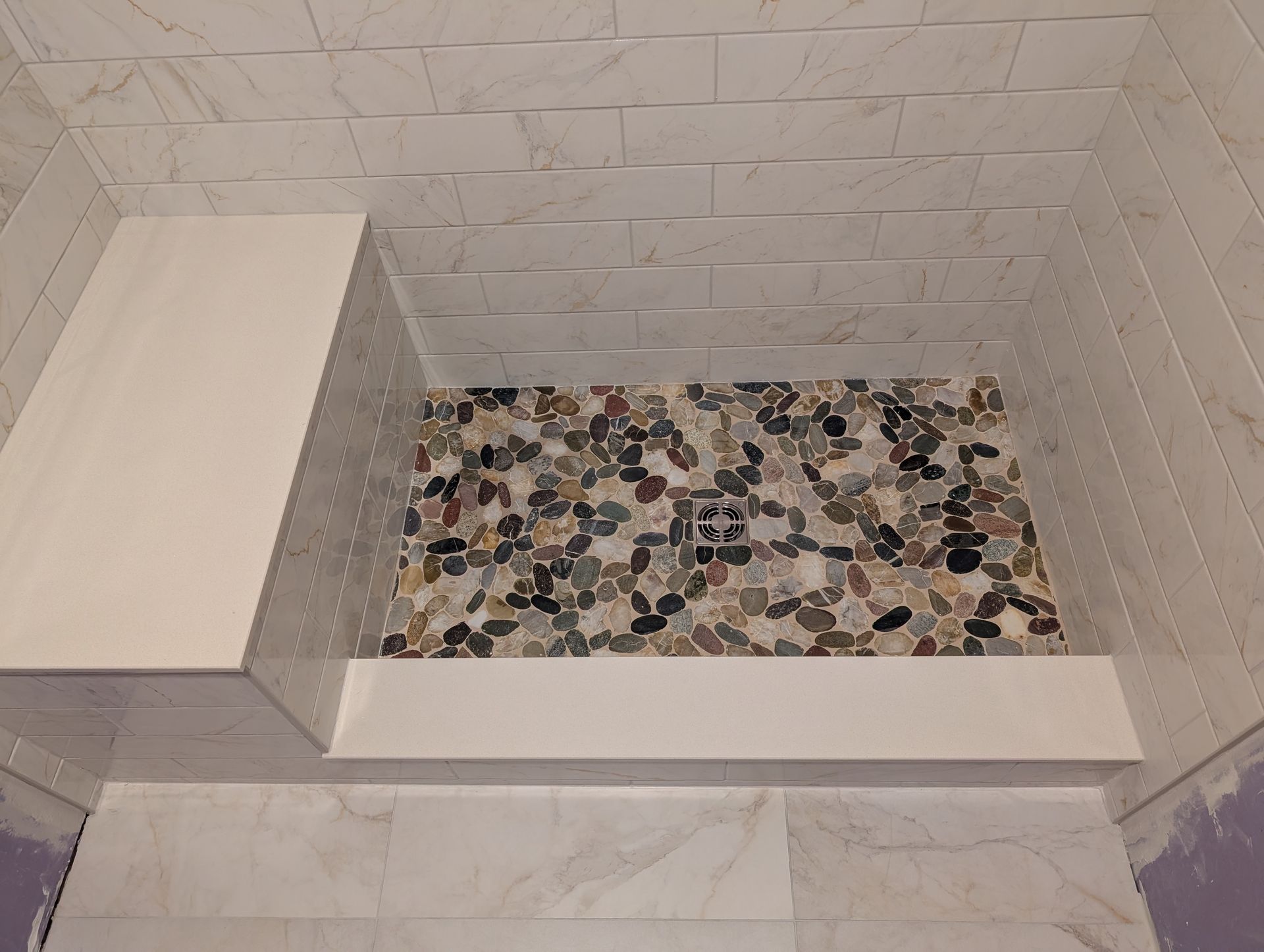 A tiled walk-in shower with a built-in bench, a pebble-stone floor, and a white threshold.
