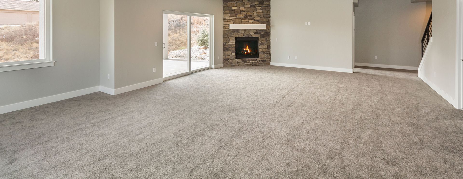 Empty living room with gray carpet, stone fireplace, and sliding glass door.