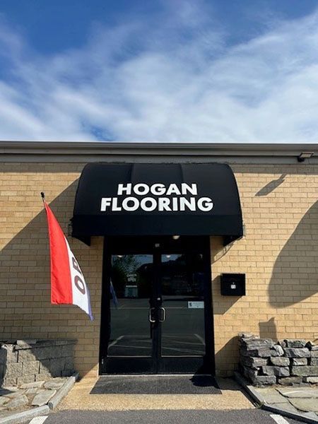 Hogan Flooring storefront with black awning and door, red and white flag, brick building.