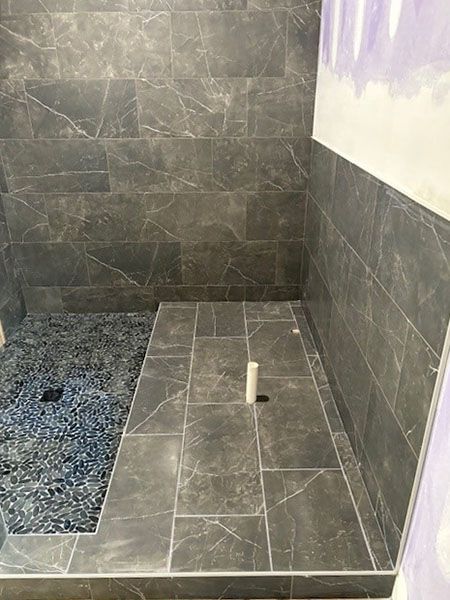 Finished tiled shower with dark grey marble-look tiles and a pebble-tiled floor.