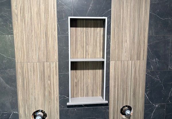 Built-in shower shelf with two shelves, white frame, wood-look backing, flanked by tiled wall sections and fixtures.