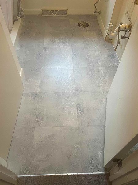 Gray tiled floor in a narrow hallway, with white walls on either side and doorway entrances.