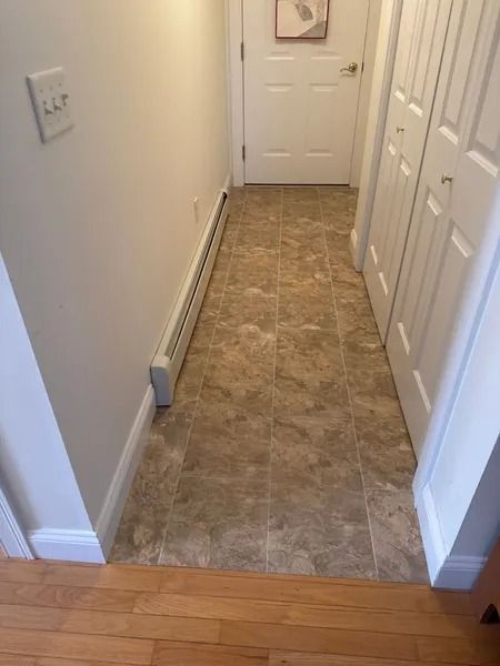 Narrow hallway with beige tile floor, white walls, door, and closet.