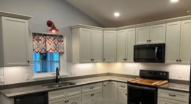Kitchen with pale green cabinets, black appliances, and a patterned window treatment.
