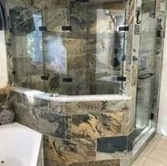 Shower with glass doors, stone tile walls. White tub partially visible.