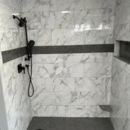 Marble-tiled shower with dark gray accent stripe and fixtures. Built-in shelf and corner seat.