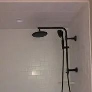 Black showerhead and handheld shower fixture on white tiled wall.