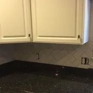 Cream kitchen cabinets above a black granite countertop with dark gray herringbone tile backsplash.