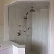 Modern shower with glass door, built-in bench, and silver fixtures. Light-colored tiled walls.