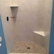 Tiled shower with a corner seat and shelf, featuring a mosaic floor.