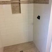 Shower with white tile walls, a recessed shelf with brown tile, and a gray tile floor.