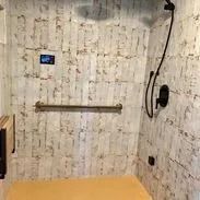 Shower with light wood-look wall panels, black fixtures, a long grab bar, and a bench seat.