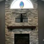 Fireplace with stone facade, stained wood mantel, and a TV mount. Arched window above with stained glass.