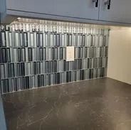 Kitchen backsplash with rectangular, alternating black, white, and gray tiles, under cabinet lighting, and dark countertop.