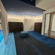 Modern office waiting area with blue and black carpet, a blue ottoman, and dark brown cabinets.