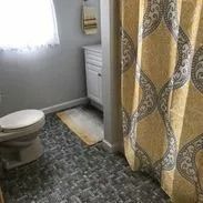 Bathroom with gray walls, patterned floor, white toilet, yellow shower curtain, and small vanity.