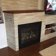 Fireplace with wood mantel and light tile facade, adjacent to shelves and TV.