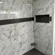 Bathroom shower with marble-like tiles, dark gray horizontal band, recessed shelf, and gray floor.