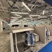 Office space with cubicles, adjustable desk, and patterned ceiling.