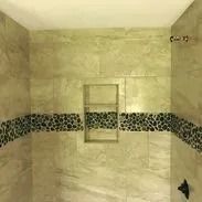 Beige tiled shower with pebble accent band and recessed shelf.