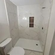 White tiled bathroom with a toilet and shower stall.