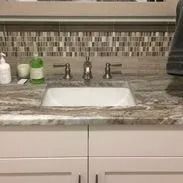 Bathroom sink with white cabinet, stone countertop, and mosaic tile backsplash.