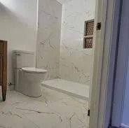 Bathroom with white marble-patterned tile, a toilet, a shower, and a built-in niche.