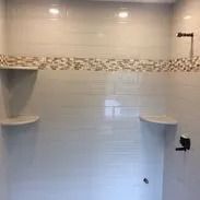 White tiled shower with mosaic accent, built-in shelves, and dark fixtures.