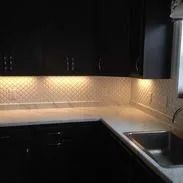 Black kitchen cabinets with lit backsplash and countertops.