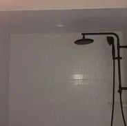 Shower with dark bronze fixtures against white tile wall.