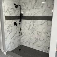 Shower with marble-look tiles, dark gray accent strip, and dark gray shower base. Black shower fixtures.