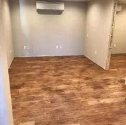Empty room with wood-look flooring and gray walls. Air conditioning unit is mounted on the ceiling.