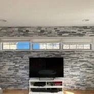 TV on a white stand against a stone-patterned wall with windows above.