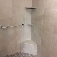 Tiled shower with corner shelves and a grab bar. Gray and white tones.