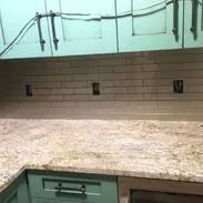 Kitchen with beige tile backsplash, granite countertop, and teal cabinets. Electrical outlets visible.