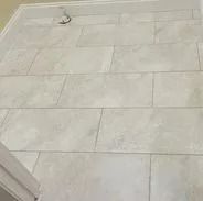 Light-colored tile floor in a bathroom; rectangular tiles arranged in a staggered pattern.