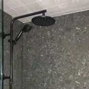Black shower head and handheld shower against gray tiled wall.